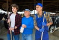 Positive elderly cow breeder with adult son and teenage grandson in cowshed