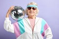 Positive elderly lady holds sparkling disco ball, dressed smiling at camera. Royalty Free Stock Photo