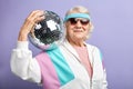 Positive elderly lady holds sparkling disco ball, dressed smiling at camera. Royalty Free Stock Photo