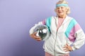 Positive elderly lady holds sparkling disco ball, dressed smiling at camera. Royalty Free Stock Photo