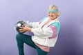 Positive elderly lady holds sparkling disco ball, dressed smiling at camera. Royalty Free Stock Photo