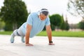 Positive elderly man athlete headphones and sportswear doing push ups outside in city park Royalty Free Stock Photo