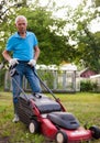 Positive elderly man with lawnmower when mowing the lawn Royalty Free Stock Photo