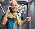 Positive elderly passenger talking on mobile phone in subway car