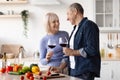 Positive elderly spouses drinking red wine while preparing meal Royalty Free Stock Photo