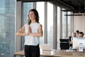 Positive employee doing yoga standing in coworking office during