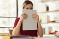 Positive employee hides face behind clipboard in office