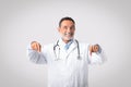 Positive european senior doctor with open mouth in white coat points finger down at copy space