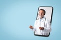 Positive european senior doctor in white coat with stethoscope, headphones on big screen phone