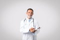 Positive european senior man doctor in white coat with stethoscope make notes, enjoy work