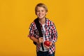 Positive european teenager boy pupil with backpack holding red apple, sharing and look at camera