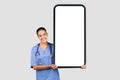 Positive european young lady surgeon or nurse in blue uniform, show big phone with blank screen