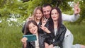 Positive family sitting together on soft plaid utdoors and taking selfie on modern smartphone. Young parents with two