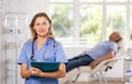 Positive female doctor standing in medical office with document folder Royalty Free Stock Photo