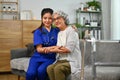 Positive female health visitor embracing elderly woman sitting on couch at home. Trust, support and health care concept Royalty Free Stock Photo