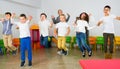 Positive female teacher and group of schoolkids jumping in classroom