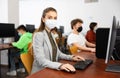 Positive female teacher wearing face mask working on computer in library. Concept of adult self education during