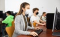 Positive female teacher wearing face mask working on computer in library. Concept of adult self education during