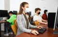 Positive female teacher wearing face mask working on computer in library. Concept of adult self education during