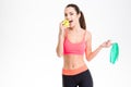 Positive fitness woman holding measuring tape and eating an apple