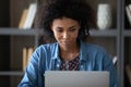 Positive focused African student girl using laptop, studying in library