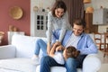 Positive friendly young parents with smiling little daughter sitting on sofa and having fun together at home Royalty Free Stock Photo