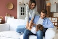 Positive friendly young parents with smiling little daughter sitting on sofa and having fun together at home Royalty Free Stock Photo