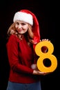 Positive girl in a Christmas Santa costume holding a number eight on a black background. 2018 concept. Royalty Free Stock Photo