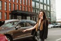 Positive girl in formal clothes stands on the road and catches a taxi with her hand raised. Cheerful young businesswoman in dark Royalty Free Stock Photo