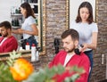 Girl hairdresser cuts hair of young man client at beauty salon Royalty Free Stock Photo