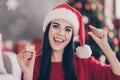 Positive girl in santa claus hat hold small gift box measure fingers in house indoors with christmas x-mas tinsels Royalty Free Stock Photo