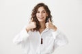 Positive good-looking caucasian adult woman showing thumbs up while being upbeat, giving aprovel and standing over gray