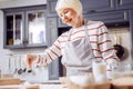 Cheerful senior woman adding flour to the dough and smiling