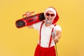 Positive grey bearded adult man in santa claus hat and pants with suspenders holding tape recorder and holding out microphone to Royalty Free Stock Photo