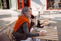 Positive grey haired senior lady talks on phone at table on outdoors cafe terrace