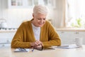 Positive grey-haired senior woman using digital tablet in kitchen