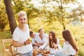 Positive guy with apple standing in front of people. Group of young people have vacation outdoors in the forest. Conception of