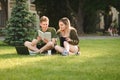 Positive guy and girl sitting on lawn in university park with books and laptop, studying with smiles on faces and talking. Royalty Free Stock Photo