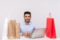 Positive handsome man sitting at desk with laptop, surrounded by packages, looking at camera smiling satisfied with shopping Royalty Free Stock Photo