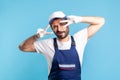 Positive handyman in overalls and hygiene gloves showing victory sign and winking playfully to camera Royalty Free Stock Photo