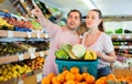 Positive family couple standing with full cart after shopping and pointing to shelves in fruit store Royalty Free Stock Photo