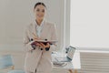 Positive happy female director in elegant wear planing working day while standing in office