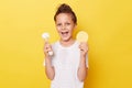 Positive happy smiling little girl with wet hair wearing casual white T-shirt standing isolated over yellow background holding Royalty Free Stock Photo