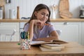 Positive happy teenage girl smiling sits at table in kitchen doing extracurricular work for school