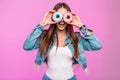 Positive happy young woman with funny smile in fashionable blue denim jacket with donuts closes eyes near vintage pink wall in Royalty Free Stock Photo