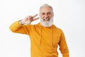 Positive hipster senior with beard and tattoos shows peave v-sign near eye, smiling and laughing happy, wearing stylish Royalty Free Stock Photo