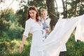 Positive housewife with hangs white clothes to dry. Young mother with her little son is outdoors in the forest. Beautiful sunshine Royalty Free Stock Photo