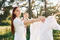 Positive housewife with hangs white clothes to dry. Young mother with her little son is outdoors in the forest. Beautiful sunshine Royalty Free Stock Photo