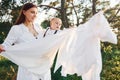 Positive housewife with hangs white clothes to dry. Young mother with her little son is outdoors in the forest. Beautiful sunshine Royalty Free Stock Photo