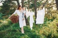 Positive housewife with hangs white clothes to dry. Young mother with her little son is outdoors in the forest. Beautiful sunshine Royalty Free Stock Photo